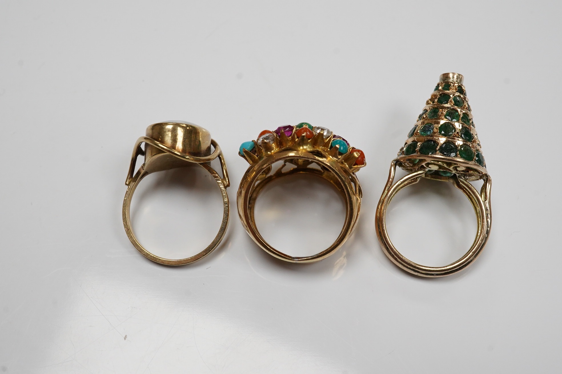 Two Indian? yellow metal and gem set rings including emerald set conical shaped and one other yellow metal and simulated opal set ring. Condition - poor to fair